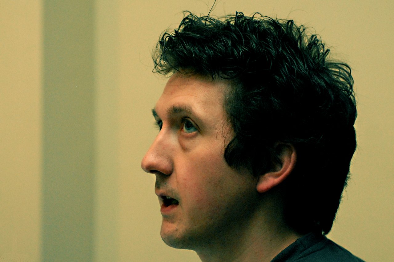 Roel de Meester A man with dark curly hair speaks while looking ahead in an indoor setting.