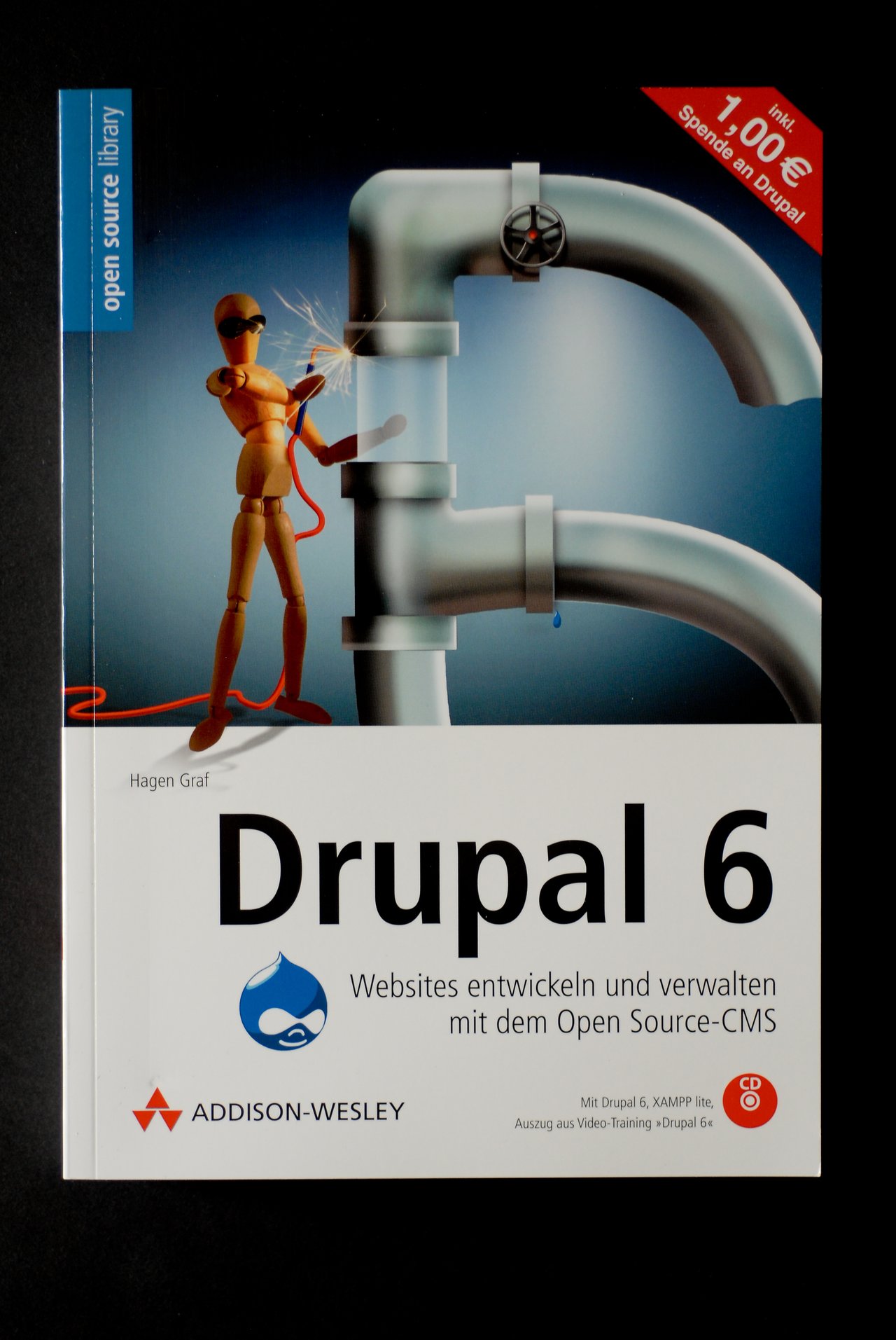Cover of the book &quot;Drupal 6&quot; by Hagen Graf, featuring a robotic figure working on a large pipe structure.