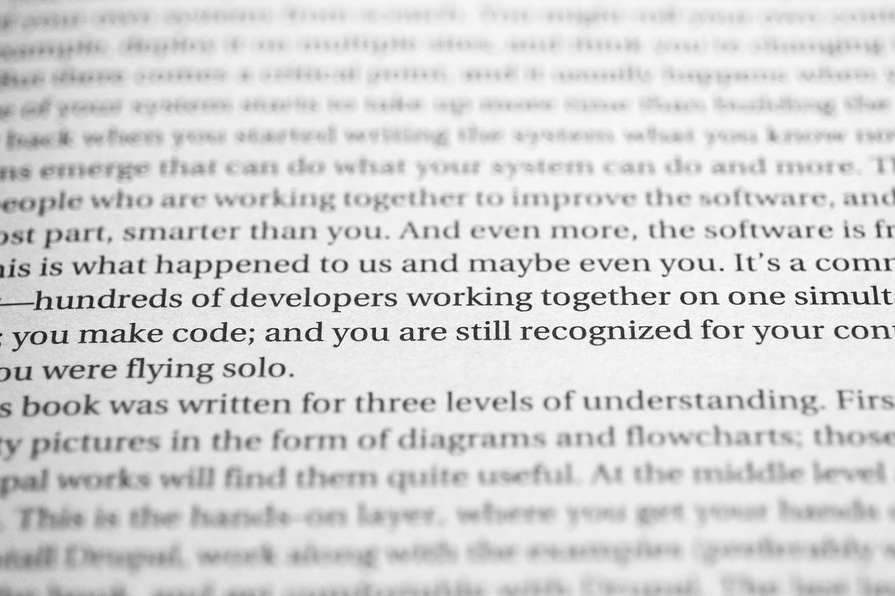 Book pro Drupal development Close-up of a book page highlighting developers collaborating on code and receiving recognition for their contributions.