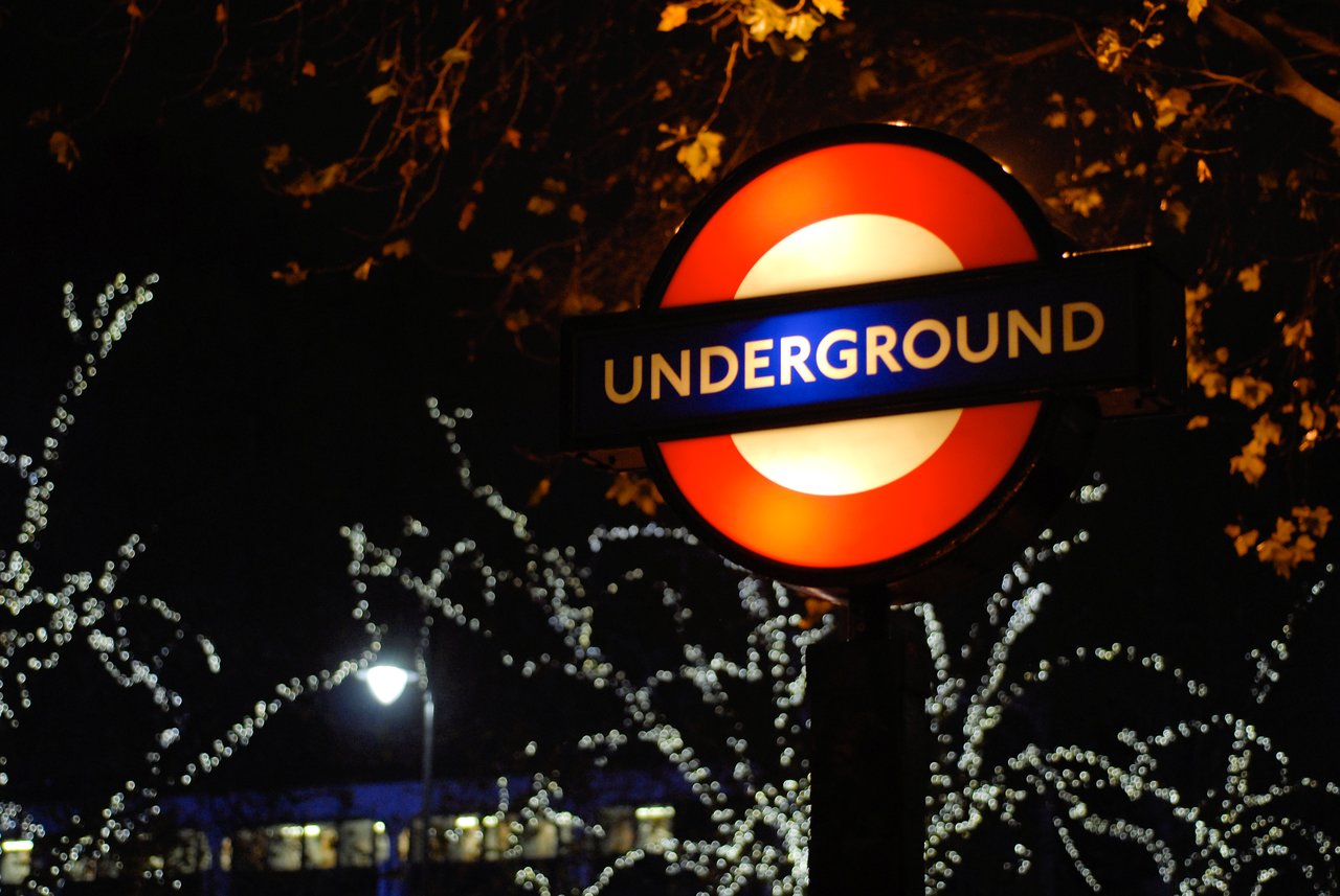 London Underground A London Underground sign glows at night, with trees and festive lights in the background.